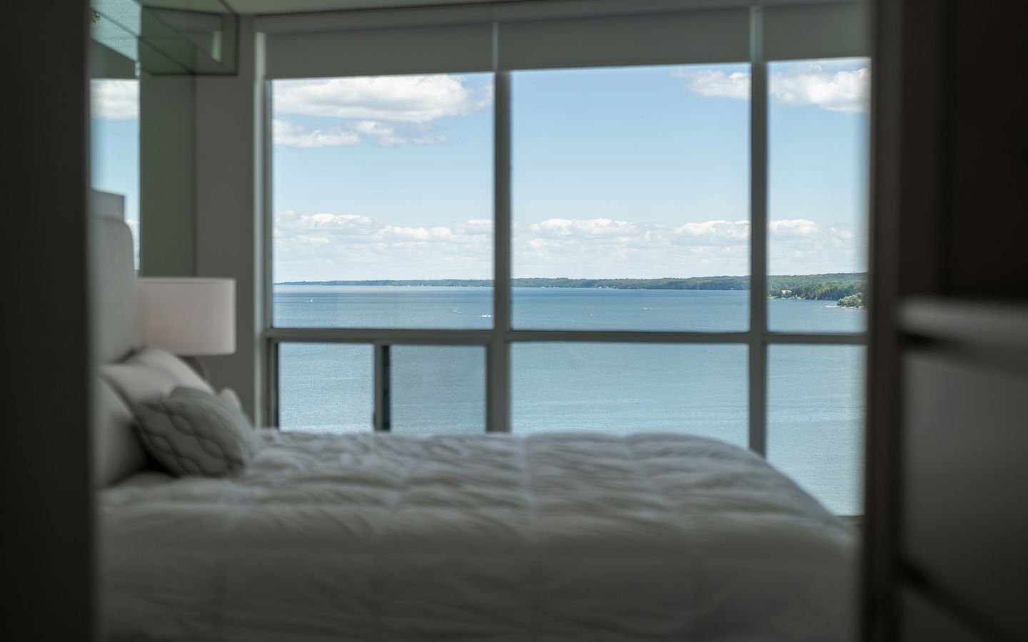 Bed with white linen facing a large window over the sea