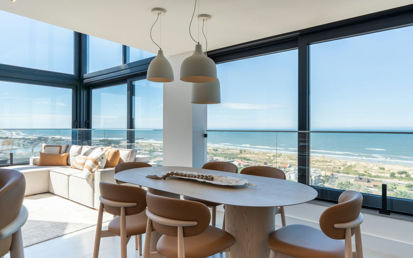 Dining table and lounge behind floor-to-ceiling windows overlooking the sea