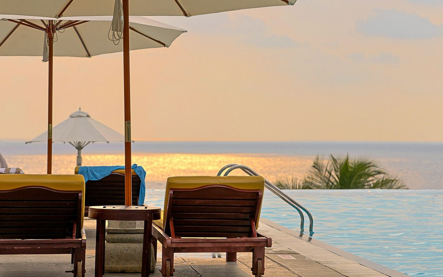 Loungers under parasols beside an infinity pool facing the sea in warm evening light