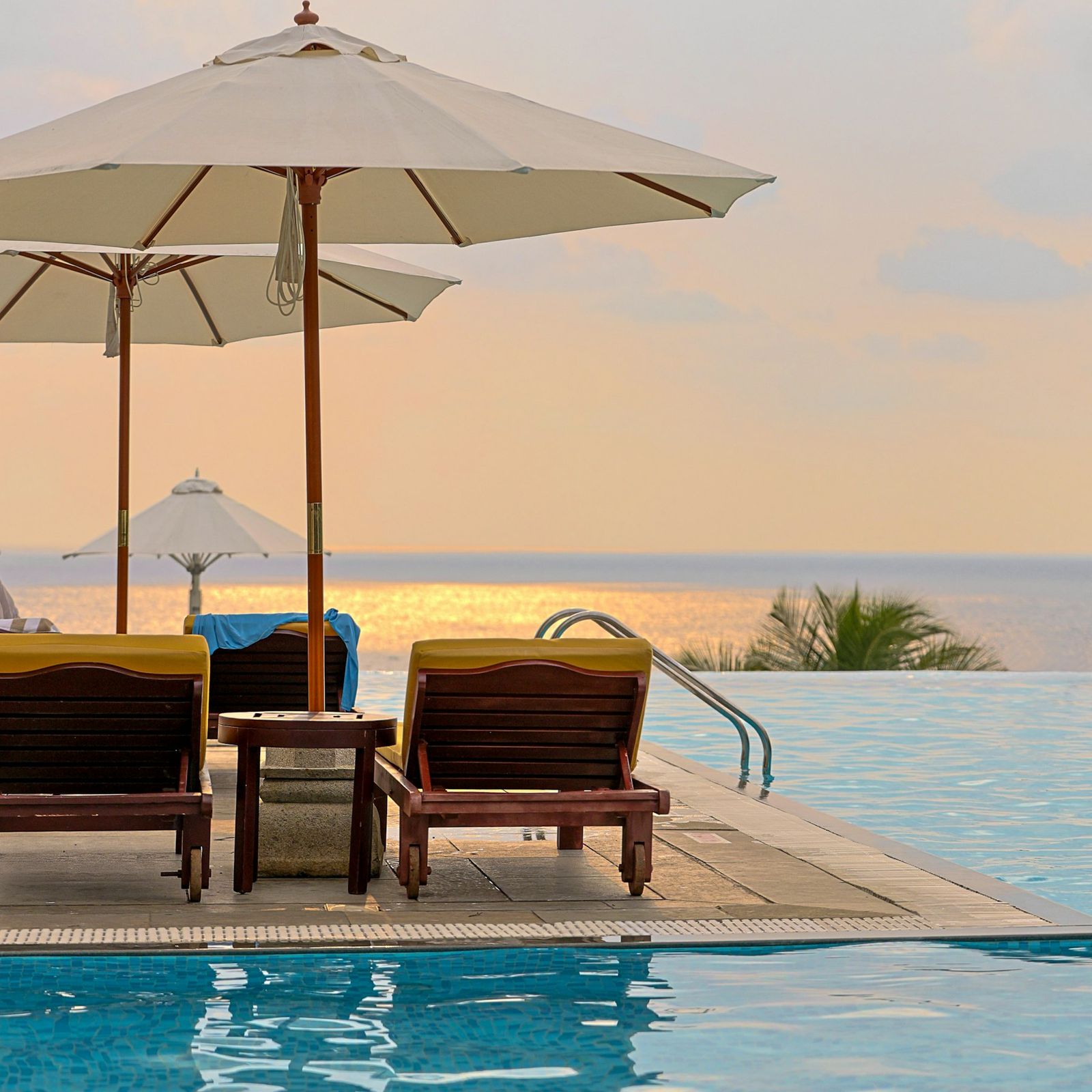 Loungers under parasols beside an infinity pool facing the sea in warm evening light