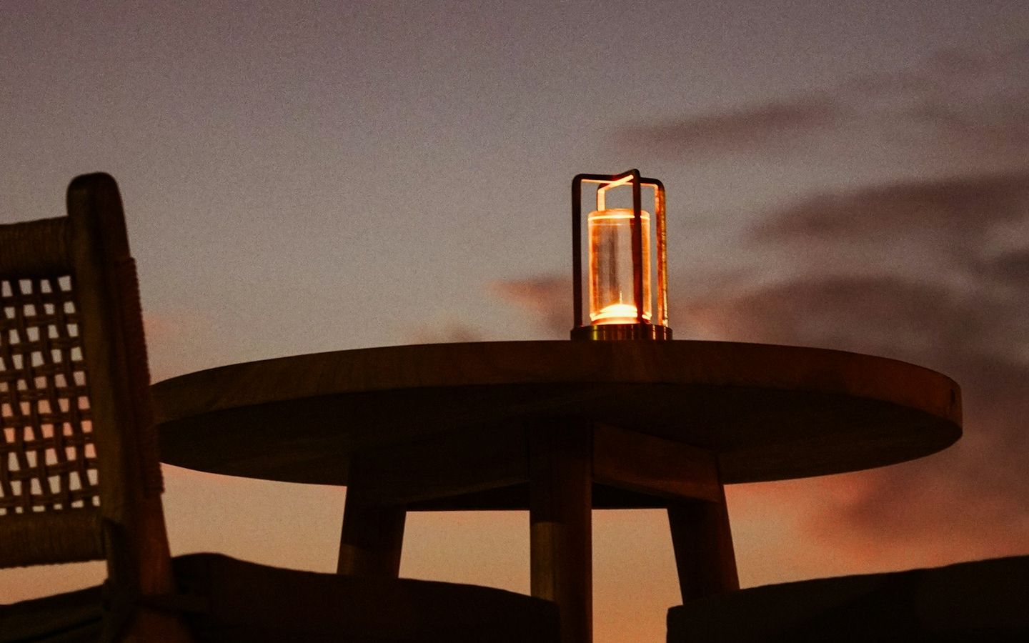 Round table with a lantern on a terrace as the sun sets over the sea