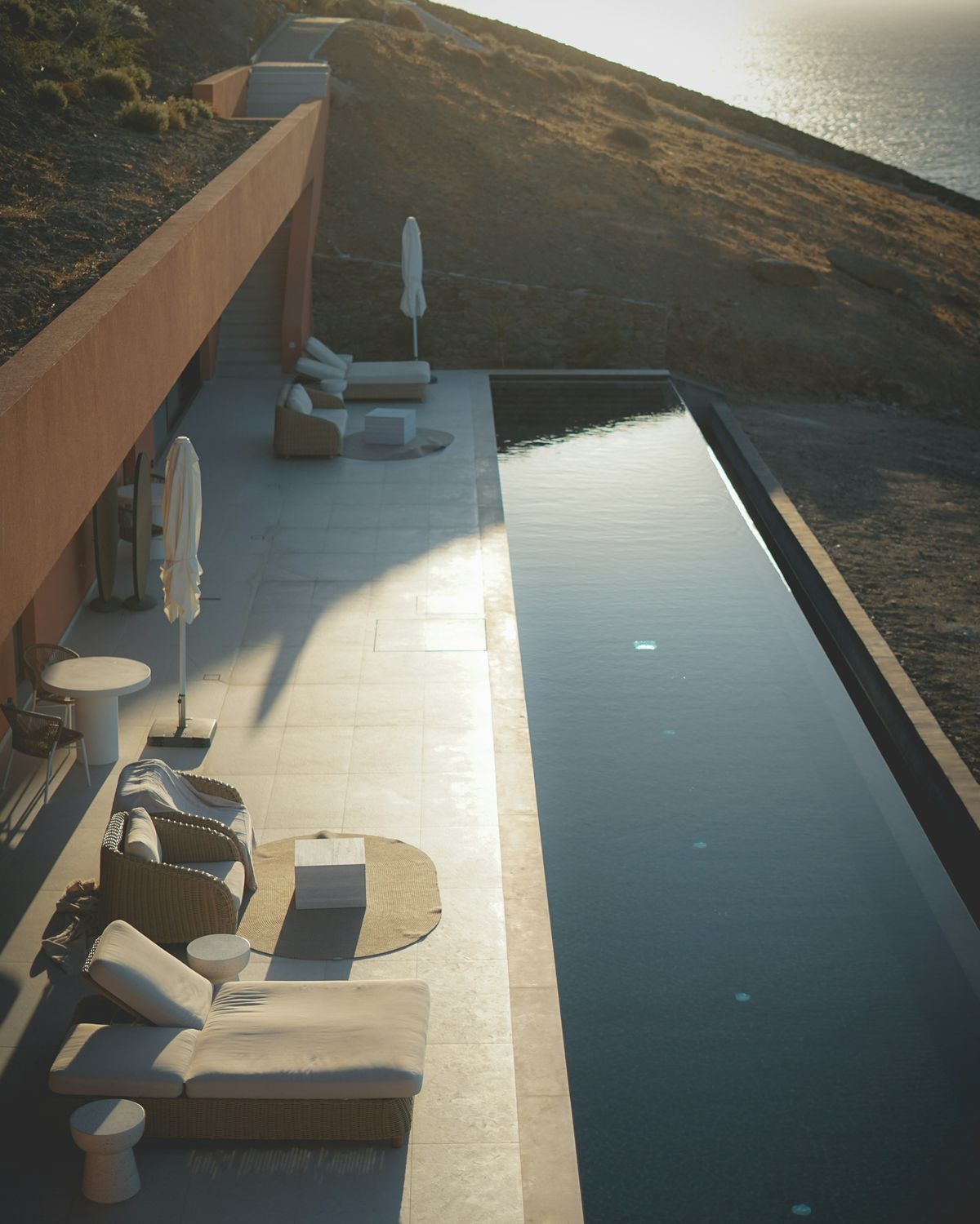 Minimal stone terrace with a narrow infinity pool and loungers at dusk