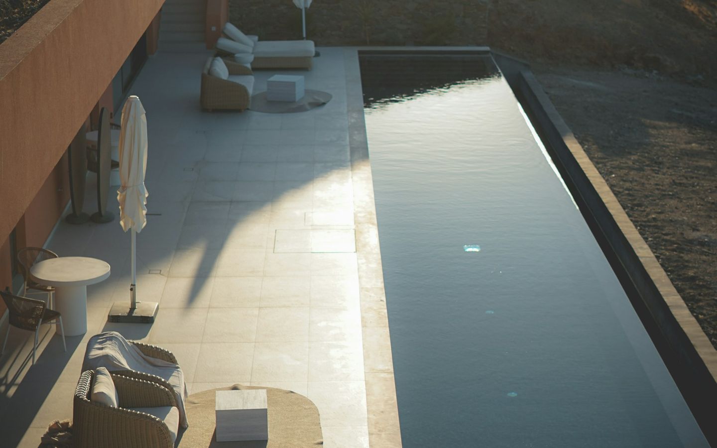 Minimal stone terrace with a narrow infinity pool and loungers at dusk
