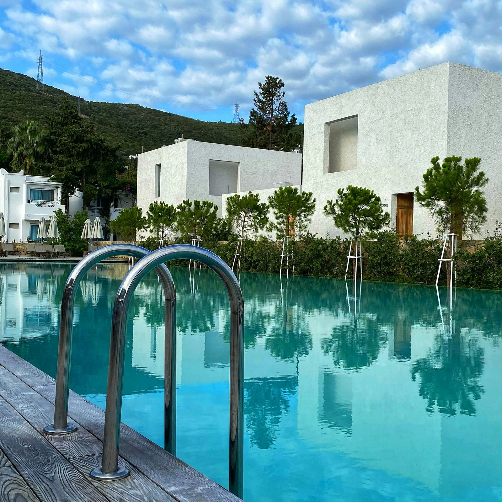White cubic villa among olive trees reflected in a long private pool