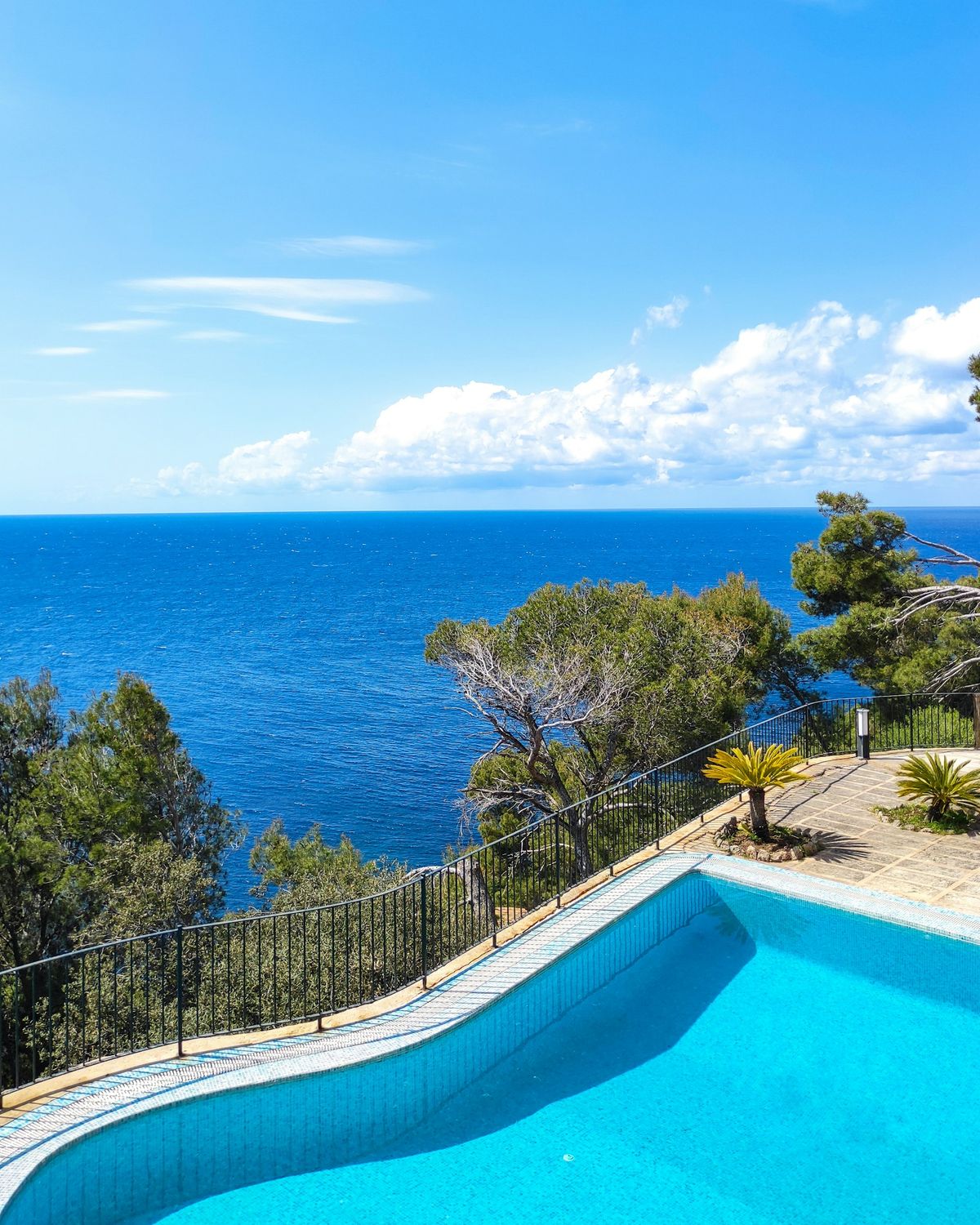 Blue pool on a stone terrace with pine trees and a wide view of the sea