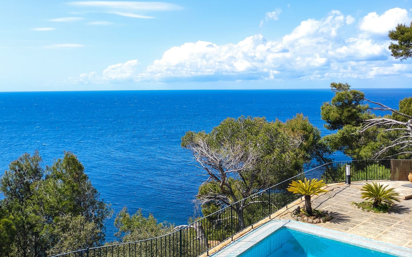 Blue pool on a stone terrace with pine trees and a wide view of the sea